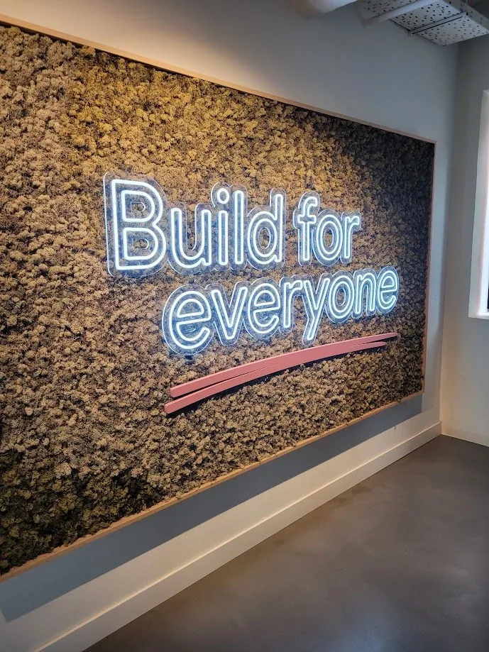 A neon sign reading Build for everyone on a moss wall at Google for Startups Campus Madrid