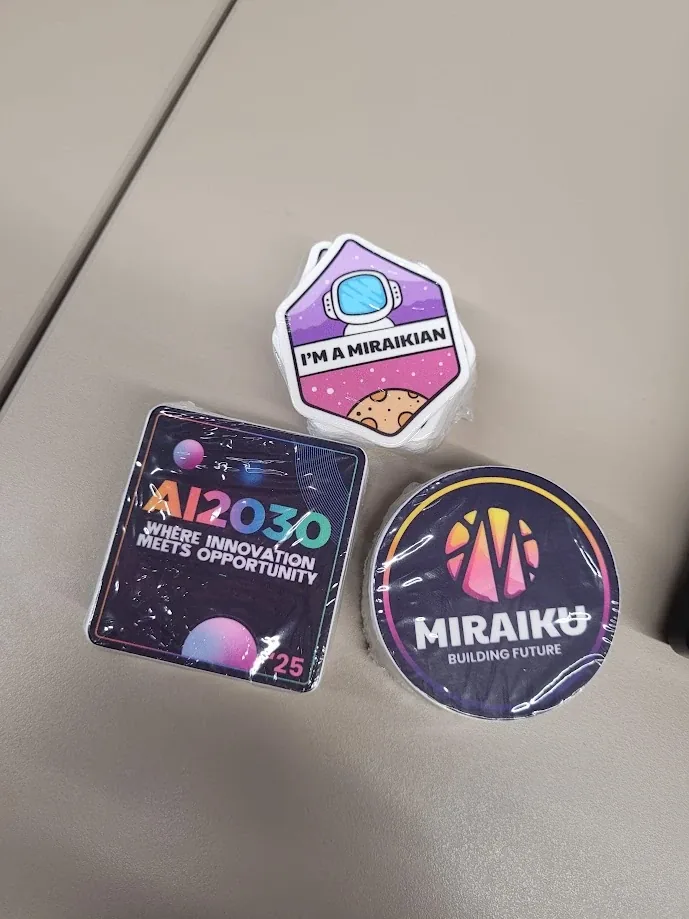 AI2030, Miraiku and I am a Miraikian stickers on a table